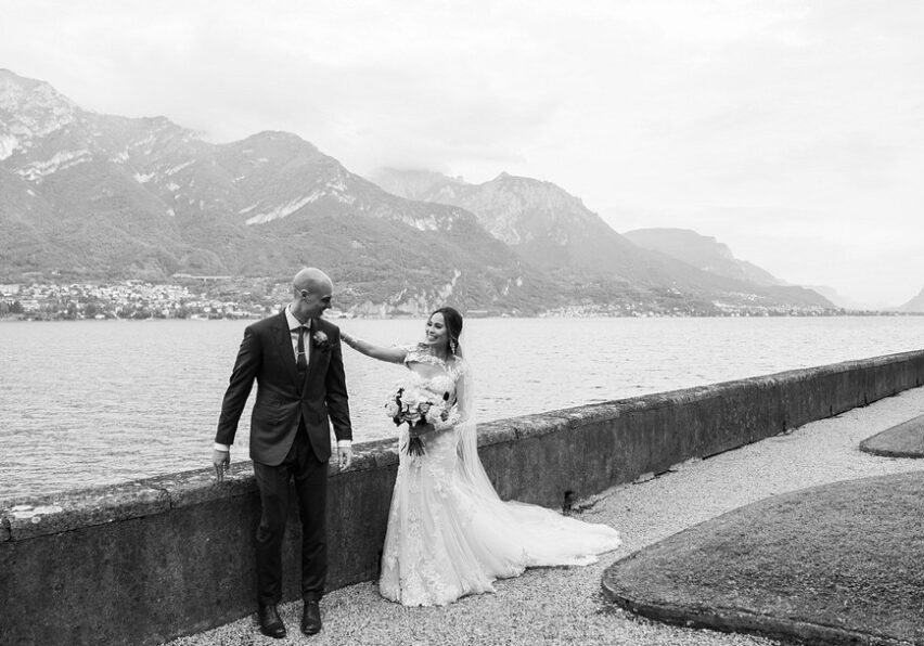 bride taps grooms shoulder for first look with Lake Como and mountains in background