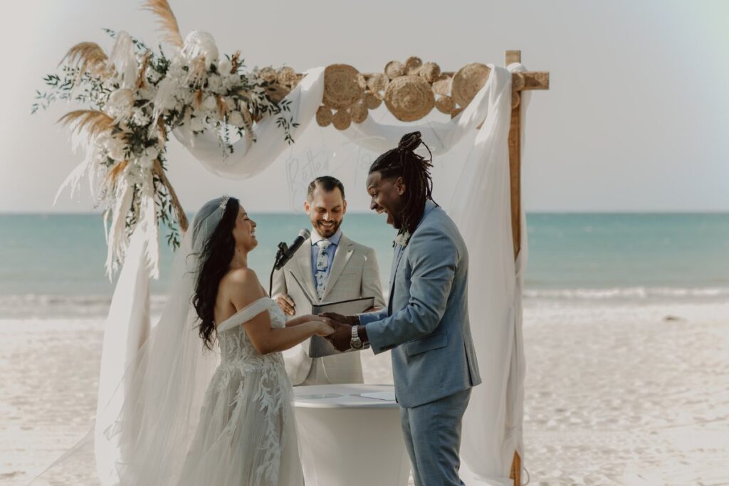 bride and groom smile at each other at the floral altar of their beach wedding