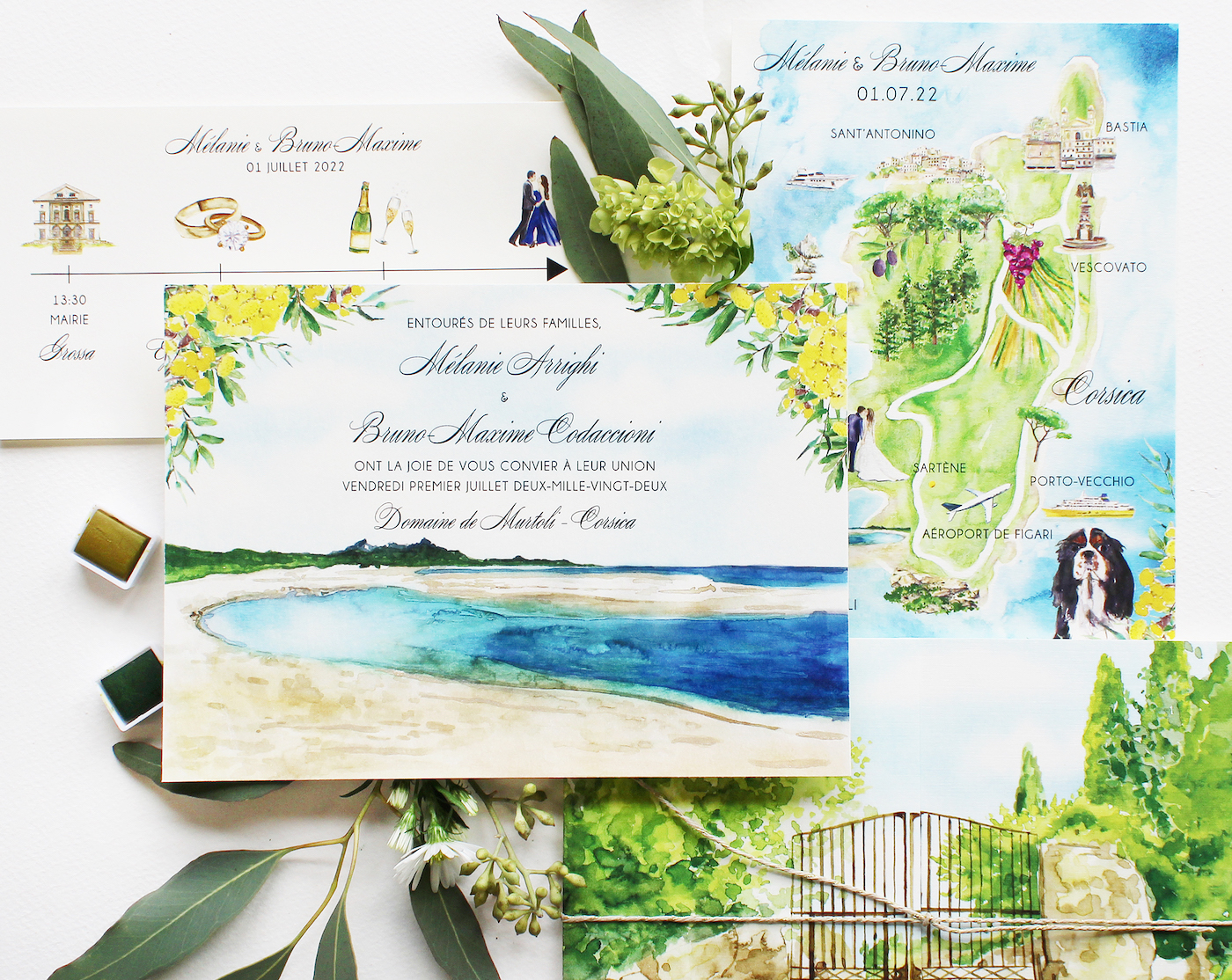 Wedding invitation set with watercolor illustrations of a coastal landscape and a map of Corsica. Includes the names "Mélanie" and "Bruno," date "01.07.22," and art materials.